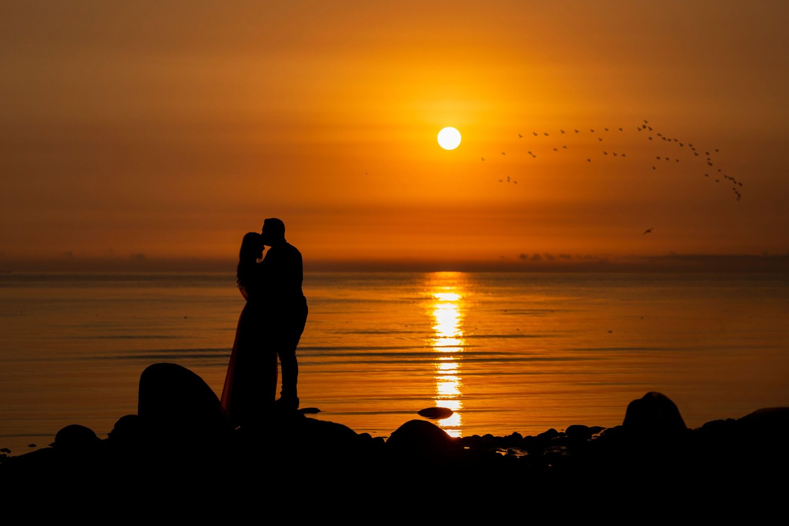 A couple silhouettes embrace during a stunning ocean sunrise.