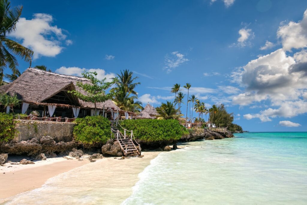Home Idyllic beachfront scene in Zanzibar with palm trees, turquoise sea, and a traditional villa.