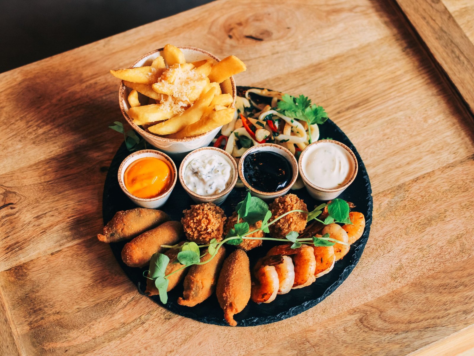 Delicious gourmet snack platter with fries, shrimp, sauces, and crispy bites on a wooden table.