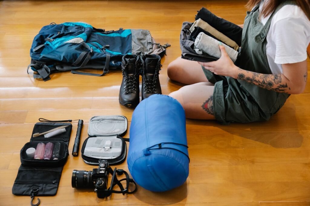 What to Pack for a Kenya Safari: The Ultimate Packing List (2026) Woman organizing Safari gear and clothes on wooden floor indoors, preparing for an adventure.