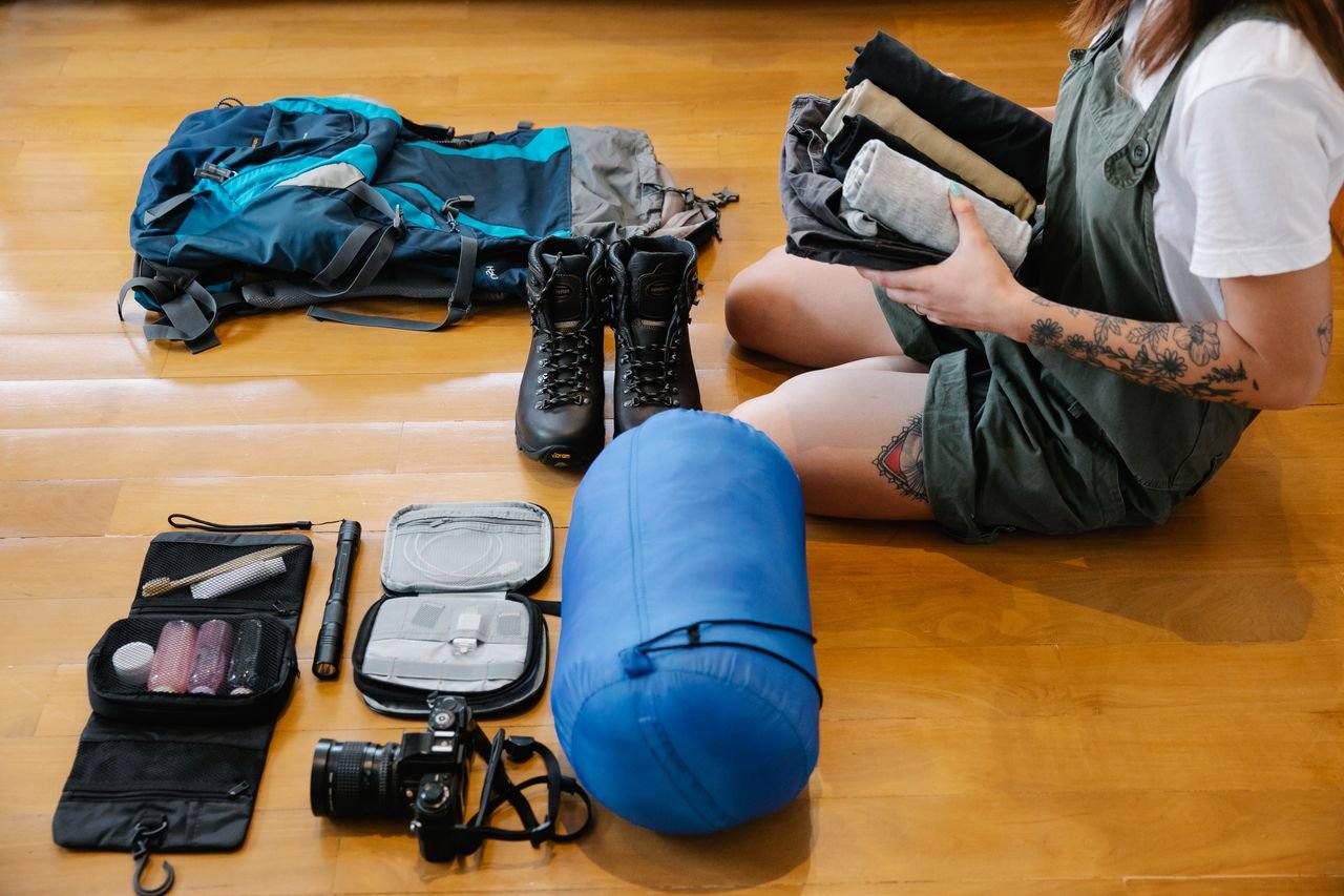 Woman organizing Safari gear and clothes on wooden floor indoors, preparing for an adventure.