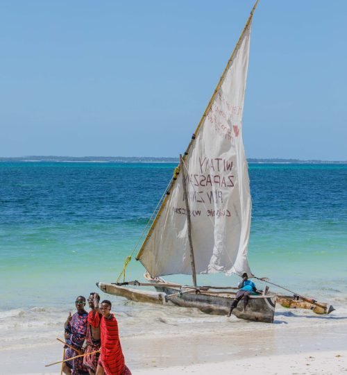 A group of Maasai people walking by a traditional sailboat on a sunny tropical beach.