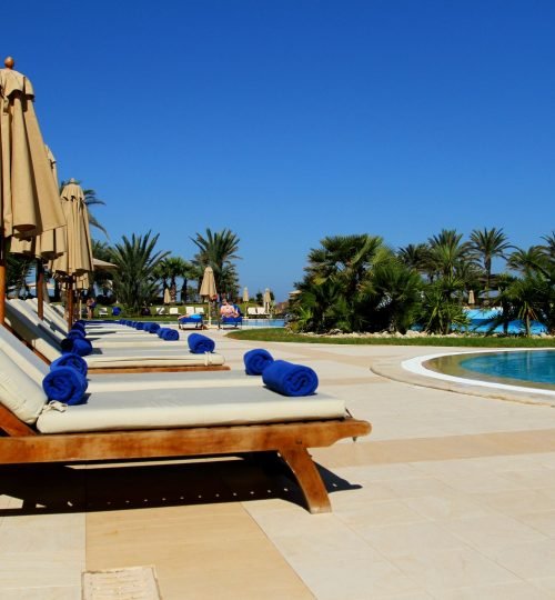 Scenic view of luxurious poolside loungers at a tropical resort under clear blue sky.